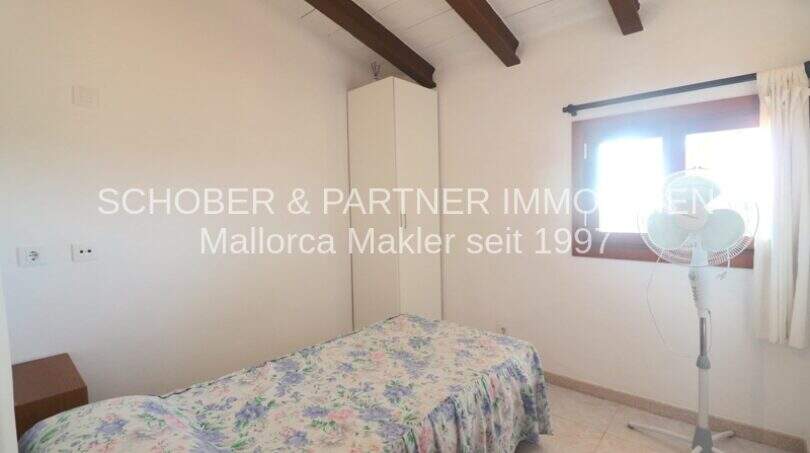 Bedroom of the Mallorca finca with single bed, white built-in wardrobe, wooden beamed ceiling and small window.