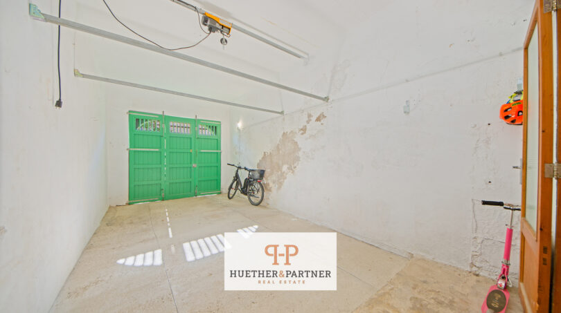 Geräumige Garage mit grünen Holztoren, weißen Wänden und Betonboden im Stadthaus Manacor