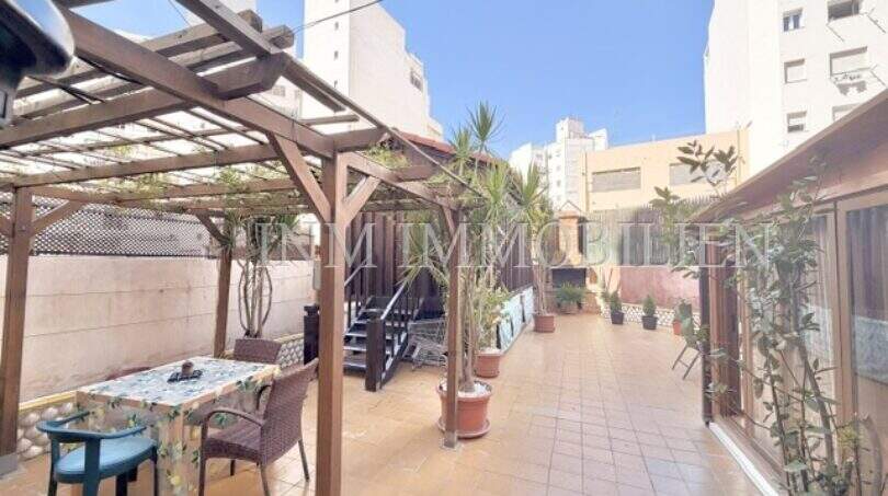Sonnige Dachterrasse mit Holzpergola, Sitzbereich und Palmen, umgeben von Stadtgebäuden in Palma