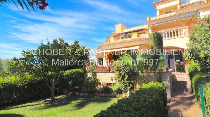 Fachada de un apartamento mediterráneo en Cala Millor con jardín privado cuidado, terraza y exuberante vegetación.