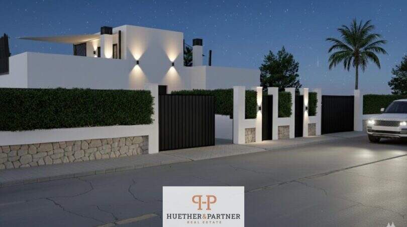 Beleuchtete Außenfassade einer modernen Neubau-Doppelhaushälfte in Cala d'Or bei Nacht mit Einfahrtstor