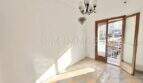 Empty living room with checkerboard floor, chandelier and balcony door in apartment needing renovation, Playa de Palma