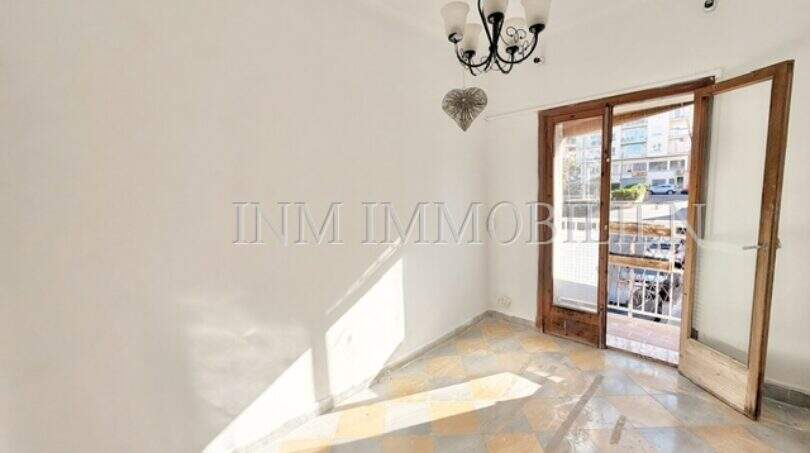 Empty living room with checkerboard floor, chandelier and balcony door in apartment needing renovation, Playa de Palma
