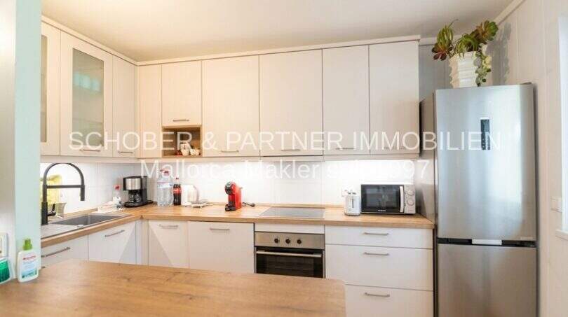 Moderne Einbauküche mit weißen Fronten, Holzarbeitsplatte und Edelstahlkühlschrank in der Wohnung in Sa Coma.