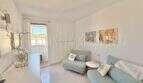 Helles Wohnzimmer mit türkisfarbener Couch, Sessel und Balkonzugang in Palmanova-Wohnung