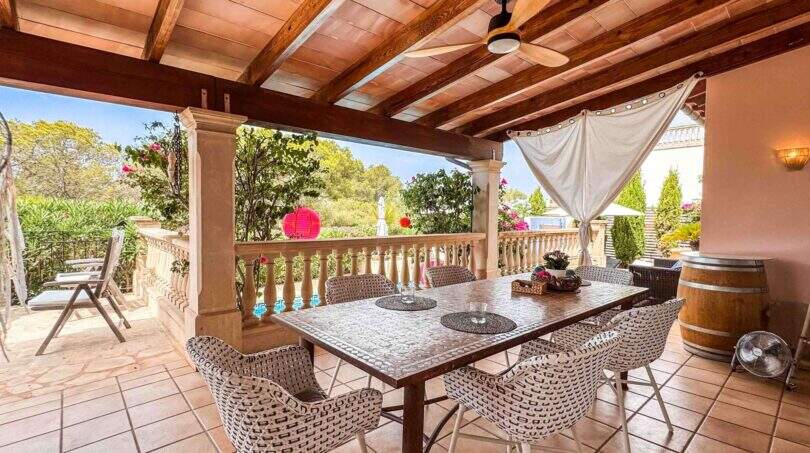 Überdachte Terrasse mit Holzdecke, Esstisch, Rattanstühlen und Blick auf üppigen Garten in Santanyí