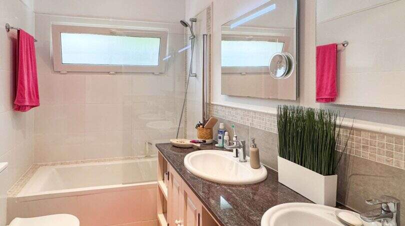 Modernes Badezimmer mit Badewanne, Dusche, Doppelwaschbecken und pinken Handtüchern im Wohlfühlhaus Santanyí