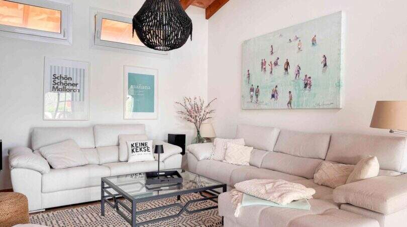 Helles Wohnzimmer mit weißen Sofas, Glasstromtisch, Strandgemälde und schwarzem Kronleuchter im Ferienhaus Santanyí
