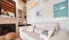 Helles Wohnzimmer mit weißem Sofa, Kamin und Holzbalkendecke im Wohlfühlhaus Santanyí