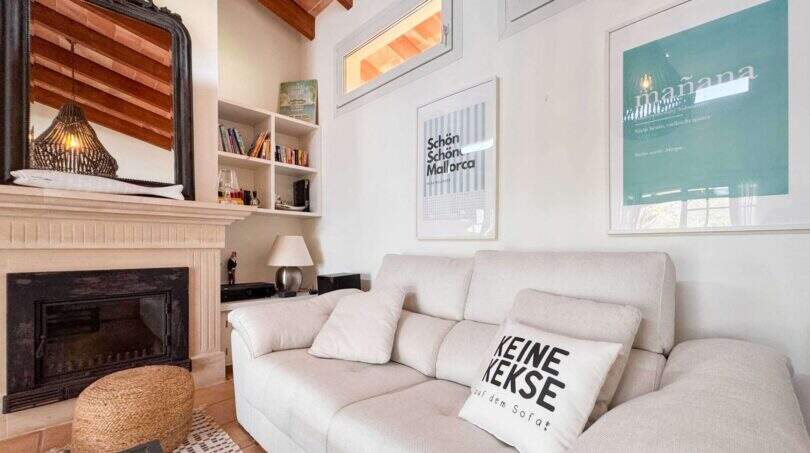 Helles Wohnzimmer mit weißem Sofa, Kamin und Holzbalkendecke im Wohlfühlhaus Santanyí