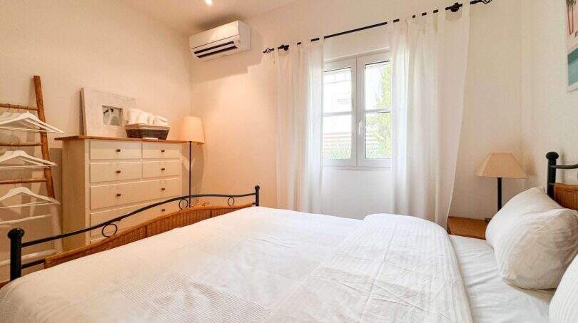 Helles Schlafzimmer mit Doppelbett, Klimaanlage, weißer Kommode und Fenster zur Gartenansicht in Santanyí