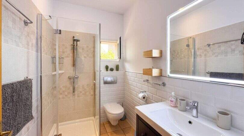 Modernes Badezimmer mit Glasdusche, Wandtoilette, beleuchtetem Spiegel und weißen Subway-Fliesen im Wohlfühlhaus Santanyí