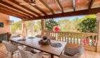 Überdachte Terrasse mit Esstisch, Rattanstühlen und Blick auf Pool und Garten der Finca in Santanyí