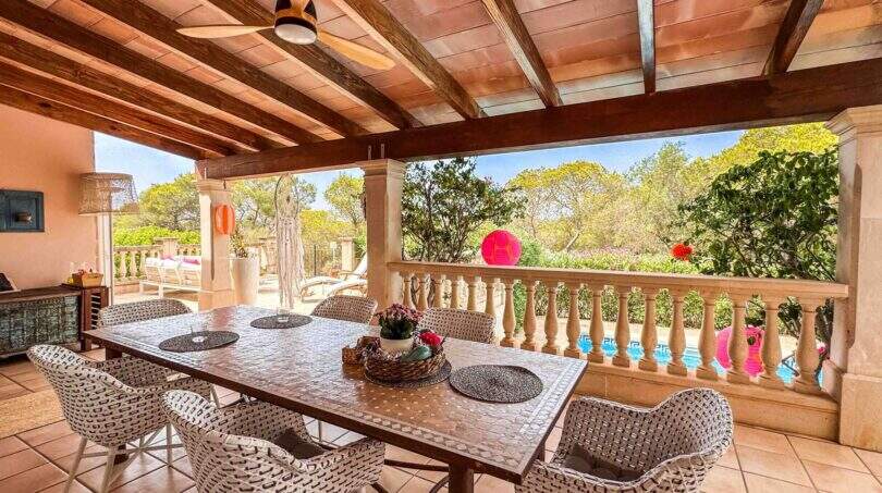 Überdachte Terrasse mit Esstisch, Rattanstühlen und Blick auf Pool und Garten der Finca in Santanyí