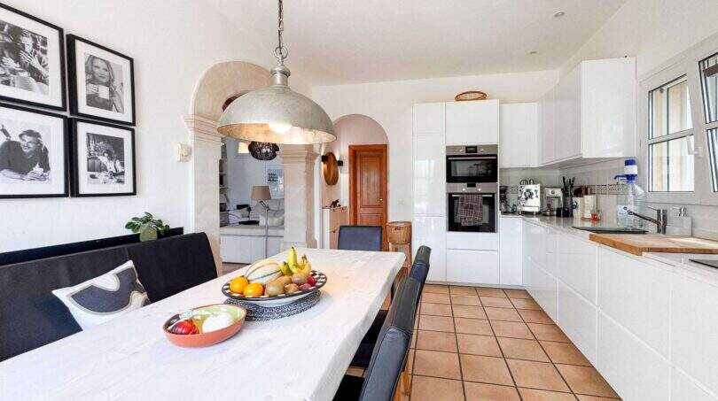 Helle Wohnküche mit weißen Fronten, Terrakottaboden, Esstisch und Rundbogen in exklusiver Villa in Santanyí