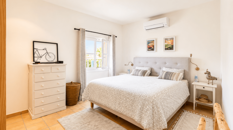 Helles Schlafzimmer mit Doppelbett, weißer Kommode, Klimaanlage und Fenster mit Meerblick in Santanyí