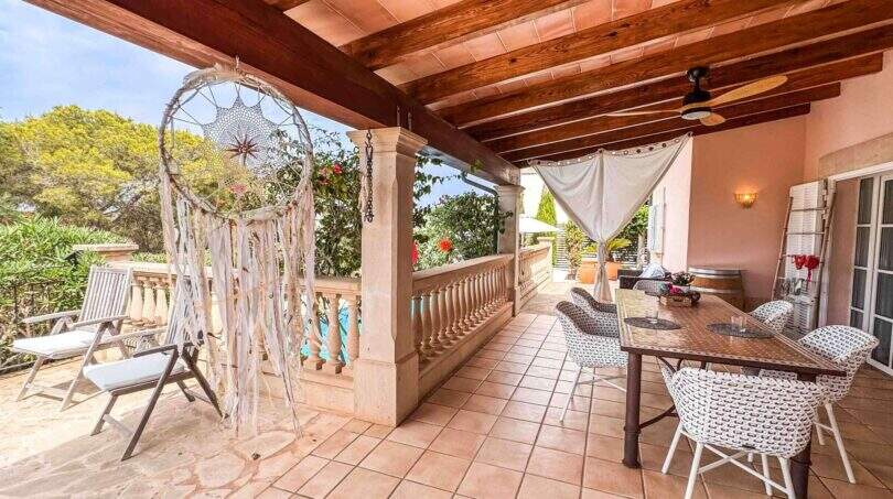 Überdachte Terrasse mit Holzbalkendecke, Traumfänger-Deko, Esstisch und Blick auf den Garten in Santanyí