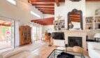 Helles Wohnzimmer mit Holzbalkendecke, Kamin, Bücherregal und Zugang zur Terrasse in Santanyí-Villa
