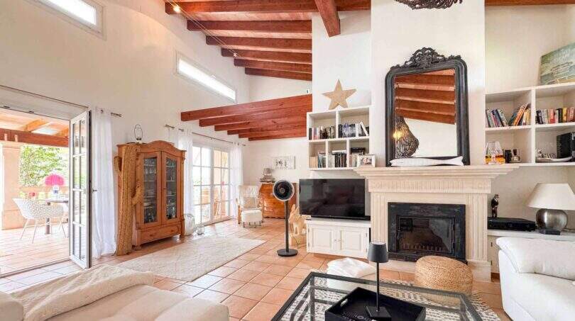 Helles Wohnzimmer mit Holzbalkendecke, Kamin, Bücherregal und Zugang zur Terrasse in Santanyí-Villa