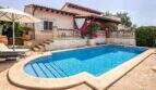 Außenbereich einer mediterranen Villa in Santanyí mit blauem Pool, Sonnenterrasse, Liegestühlen und blühenden Bougainvilleen.