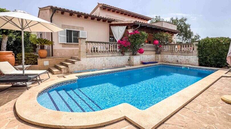 Außenbereich einer mediterranen Villa in Santanyí mit blauem Pool, Sonnenterrasse, Liegestühlen und blühenden Bougainvilleen.
