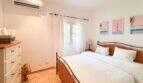 Helles Schlafzimmer mit Doppelbett, Rattankopfteil, Klimaanlage und sommerlichen Kunstdrucken in Santanyí