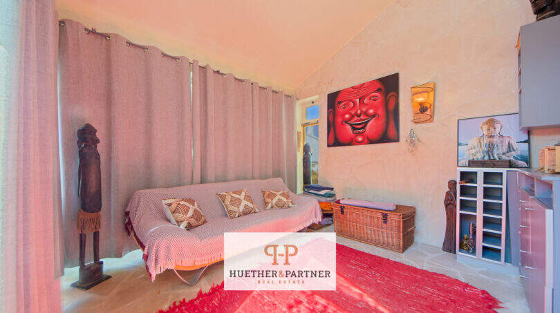 Gemütliches Wohnzimmer mit Sofa, rotem Teppich, Buddha-Kunstwerk und dekorativen Holzskulpturen in Cala Murada.