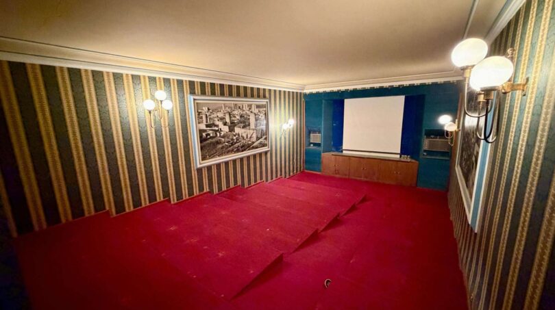 Kinoraum mit rotem Teppich, Projektionswand, Streifentapete und Wandleuchten in Retro-Villa Porto Cristo.