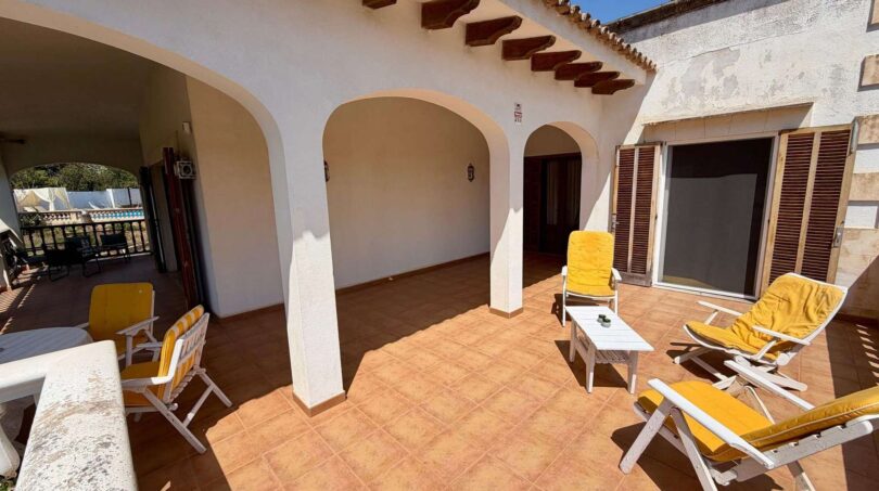 Sonnige Terrasse der Retro-Villa in Porto Cristo mit Rundbögen, Holzbalken und gelben Liegestühlen.