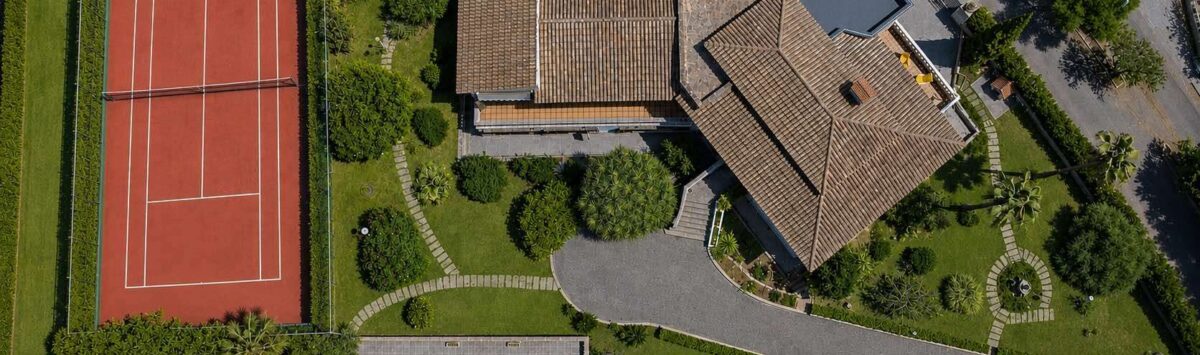 Luftaufnahme einer Villa in Porto Cristo mit Tennisplatz, Pool und gepflegtem Garten.
