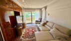 Wohnzimmer der Retro-Villa in Porto Cristo mit Ledersofa, Holzschrank, Orientteppich und Balkon mit Poolblick.
