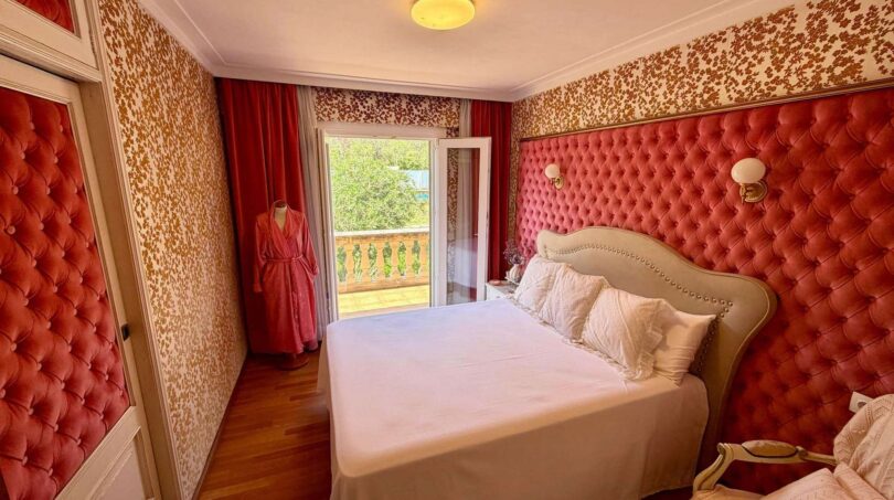 Elegantes Schlafzimmer mit rotem Samt-Kopfteil, Balkon und Retro-Tapete in Villa Porto Cristo