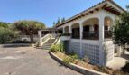 Außenansicht der Retro-Villa in Porto Cristo mit weißer Fassade, Bogenterrasse und Drachenbaum.