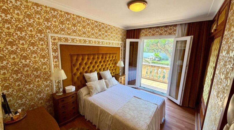 Retro-Schlafzimmer mit goldenem Polsterkopfteil, Balkonzugang und floralem Tapetenmuster in Villa Porto Cristo