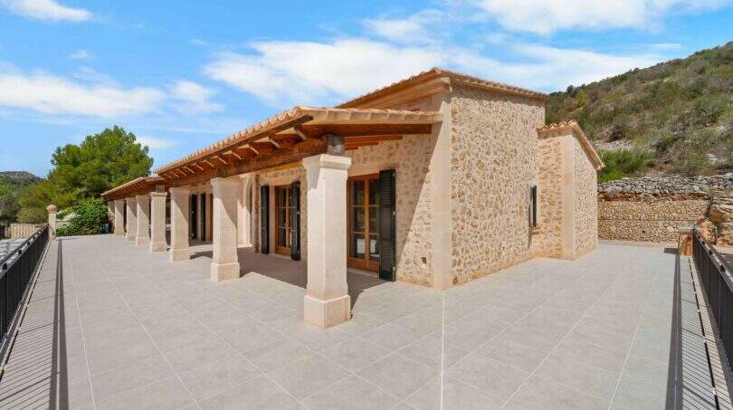 Außenterrasse der Finca in Cala Murada mit Natursteinmauern, Holzbalken-Pergola und großzügigem Fliesenboden