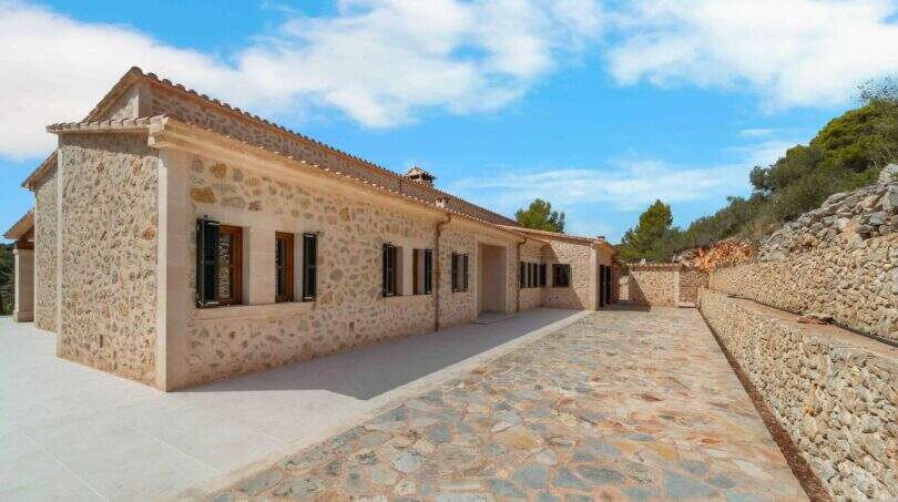 Außenansicht der mallorquinischen Finca in Cala Murada mit traditioneller Natursteinmauer und gepflastertem Innenhof.