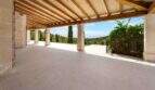 Überdachte Terrasse der Finca in Cala Murada mit Holzbalken, Natursteinpfeilern und Meerblick.