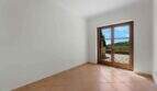 Leeres Zimmer der Finca Cala Murada mit Terrakottaboden und Glastür zum sonnigen Außenbereich mit Grünblick.