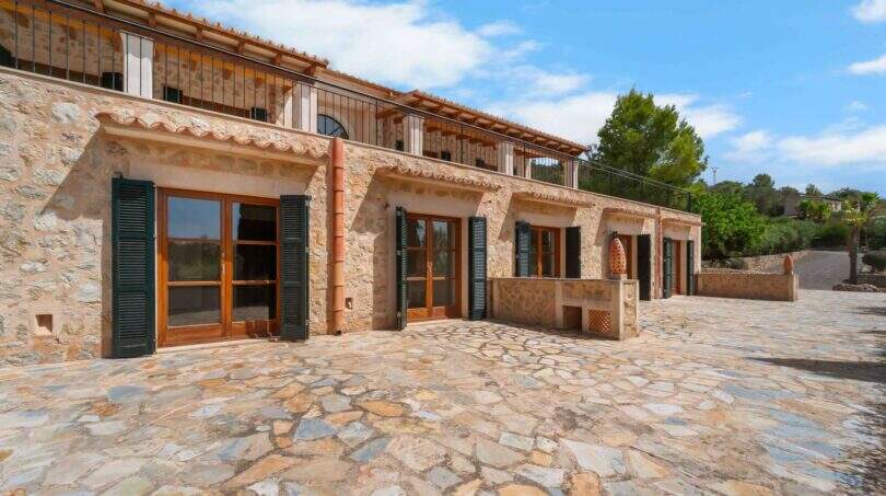 Außenansicht der Finca in Cala Murada mit Natursteinmauern, Holzfensterläden und gepflastertem Innenhof.