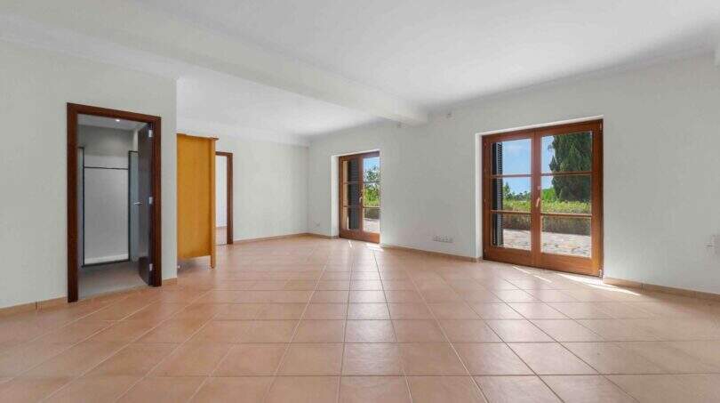 Leerer Wohnraum der Finca in Cala Murada mit Terrakottaboden und Holz-Glastüren zum Außenbereich.