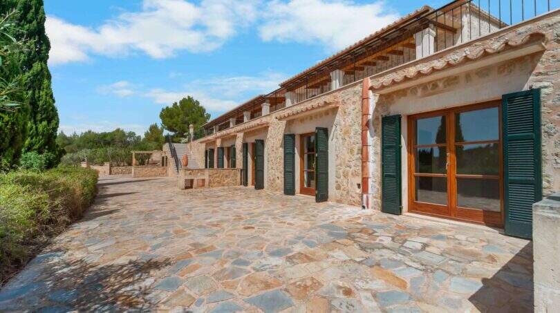 Außenansicht der Finca in Cala Murada mit Natursteinmauern, grünen Fensterläden und gepflastertem Innenhof.