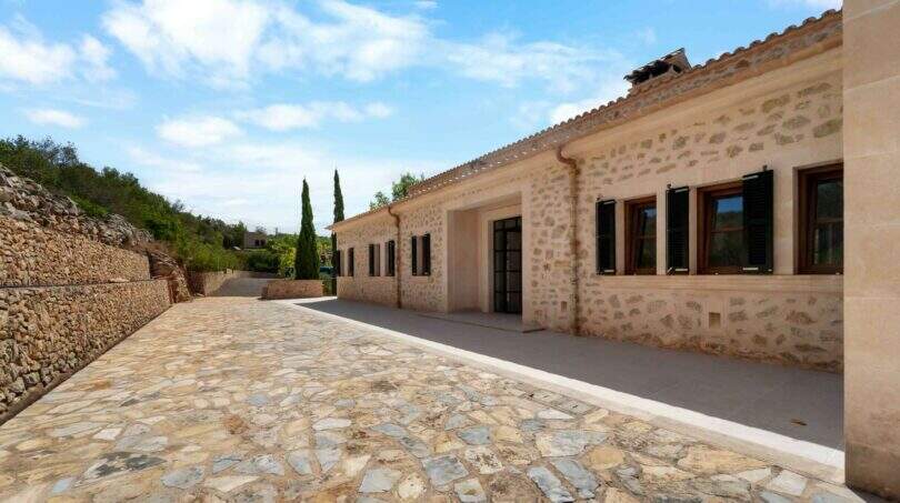 Außenbereich der Finca in Cala Murada mit Natursteinmauern, Kopfsteinpflaster und mediterranen Zypressen