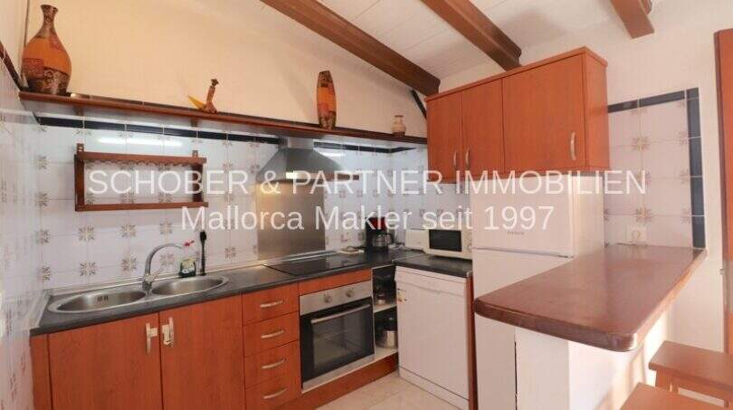Rustic built-in kitchen with wooden beam ceiling, cooking area and tile backsplash in finca on Mallorca