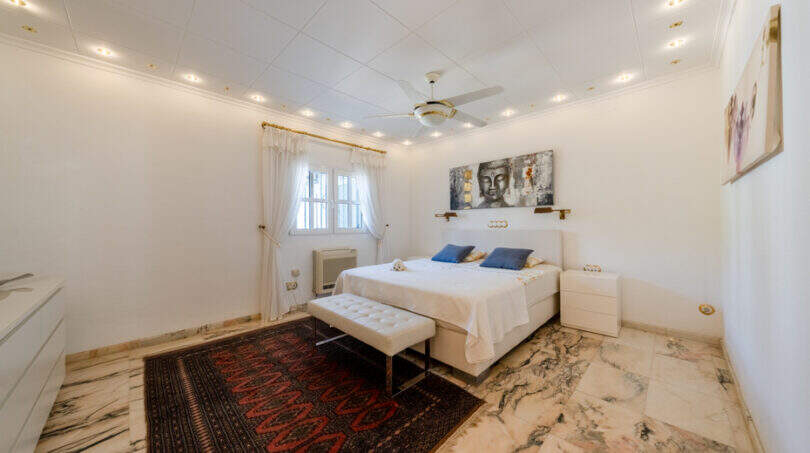 Helles Schlafzimmer mit Marmorboden, Doppelbett, Deckenventilator und Buddha-Kunstwerk in Villa Cala Murada
