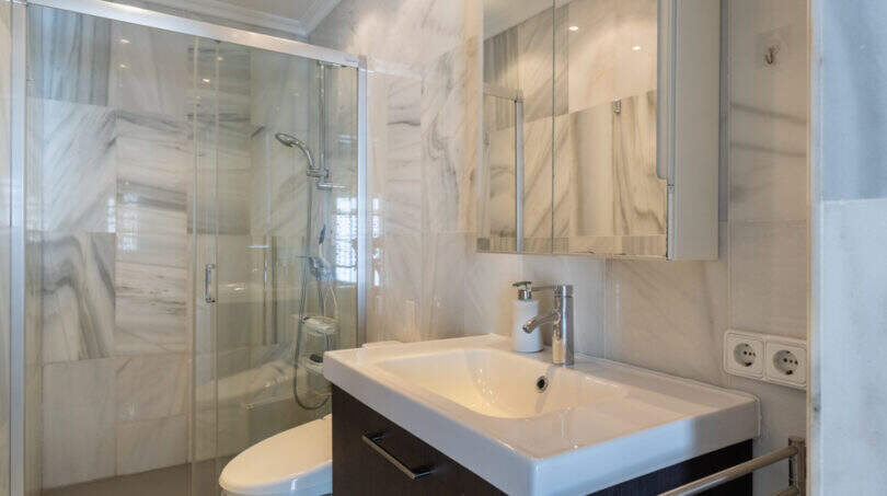 Modernes Badezimmer mit Marmorwänden, Glasdusche, Waschtisch und Spiegelschrank in Villa Cala Murada