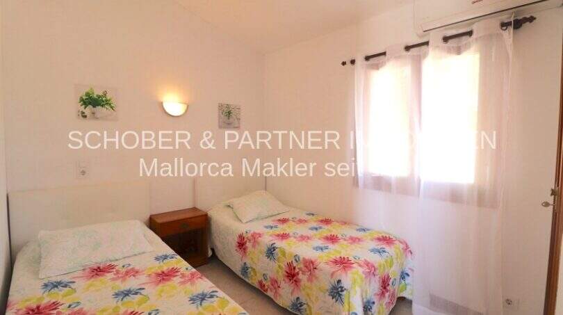Bright bedroom with two single beds, floral bedding, air conditioning and white curtains in Mallorca finca.