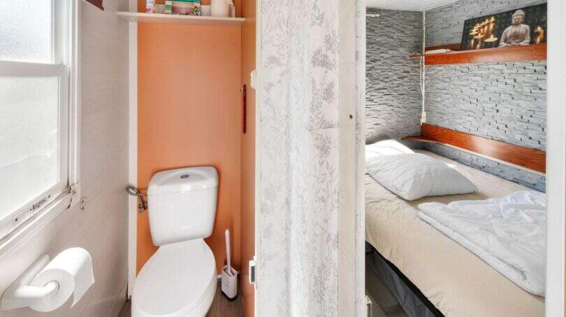 Blick ins WC mit orangefarbener Wand und angrenzendem Schlafzimmer mit Steinoptik-Tapete, Finca Algaida