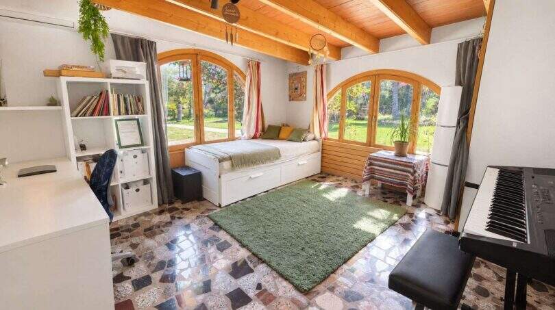 Helles Schlafzimmer der Finca Algaida mit Bogenfenstern, Holzdecke, Klaviertastatur und Blick in den Garten.