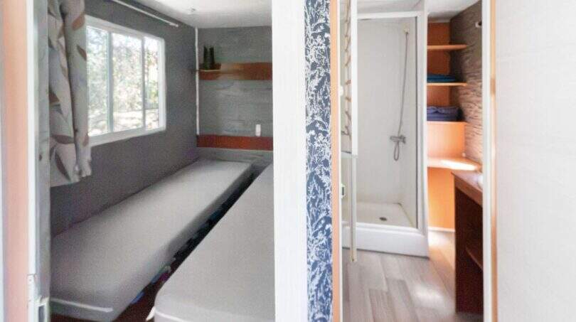 Schmales Schlafzimmer mit Einzelbett und Fenster sowie Badezimmer mit Dusche in der Finca Algaida.