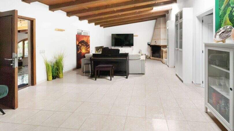 Geräumiges Wohnzimmer der Finca Algaida mit Holzbalkendecke, Kamin, Klavier und hellem Fliesenboden.